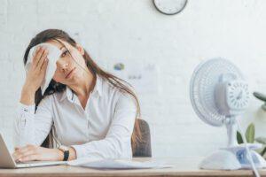 A brunette woman in her twenties in a white blouse sitting at a desk wiping off her sweat that was caused by her asking the question whether it is hard to learn German as an English speaker.